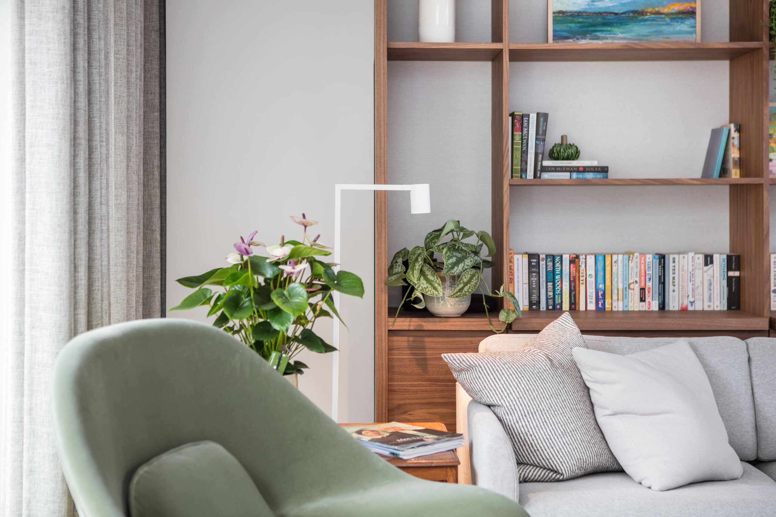 Modern living room designed by Randa Kort Interior Design in St Albans, Hertfordshire, featuring a grey sofa, green armchair, and wooden shelving.