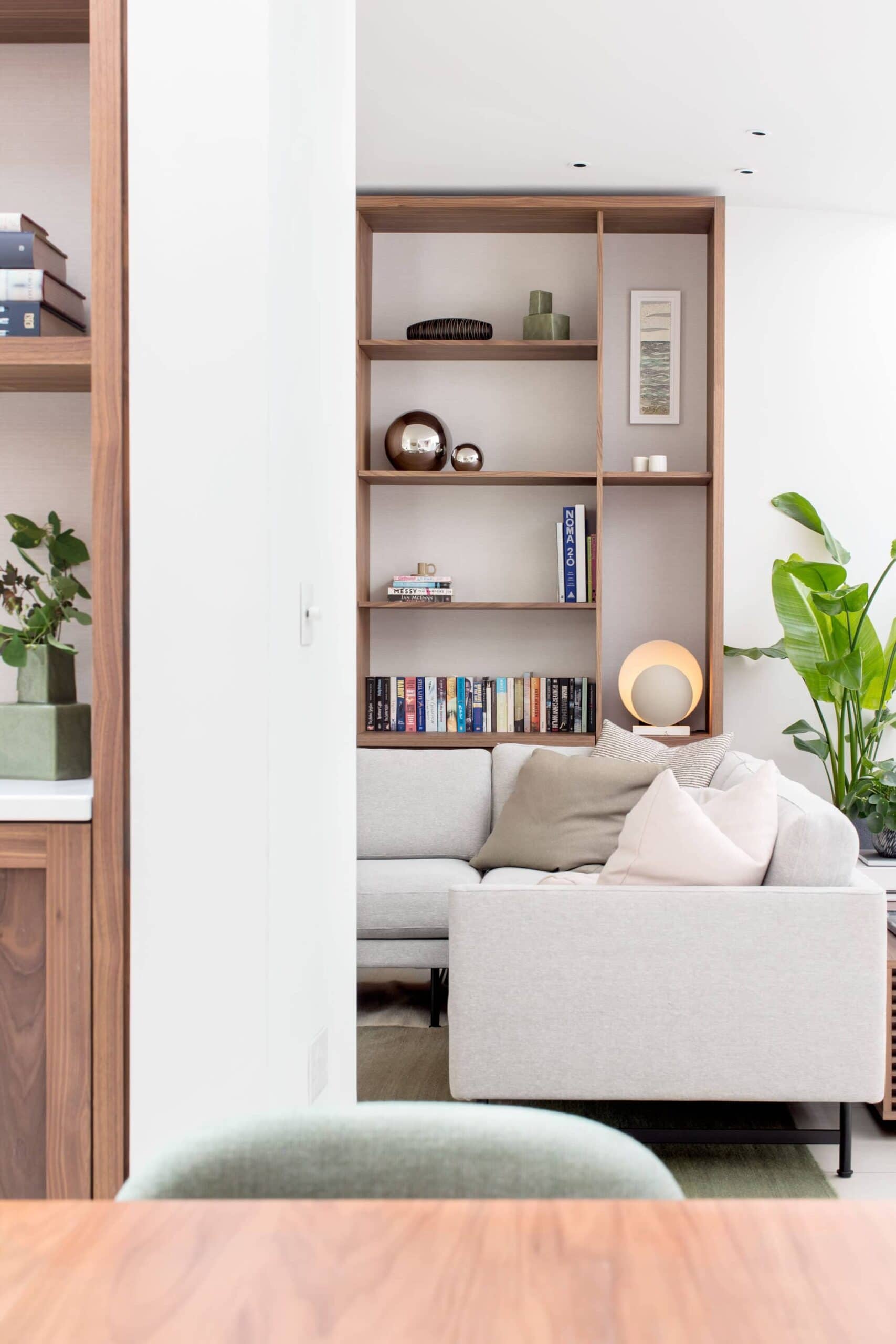 Contemporary living room designed by Randa Kort Interior Design in St Albans, Hertfordshire, featuring a sleek bookshelf, cosy sofa, and lush green plants.