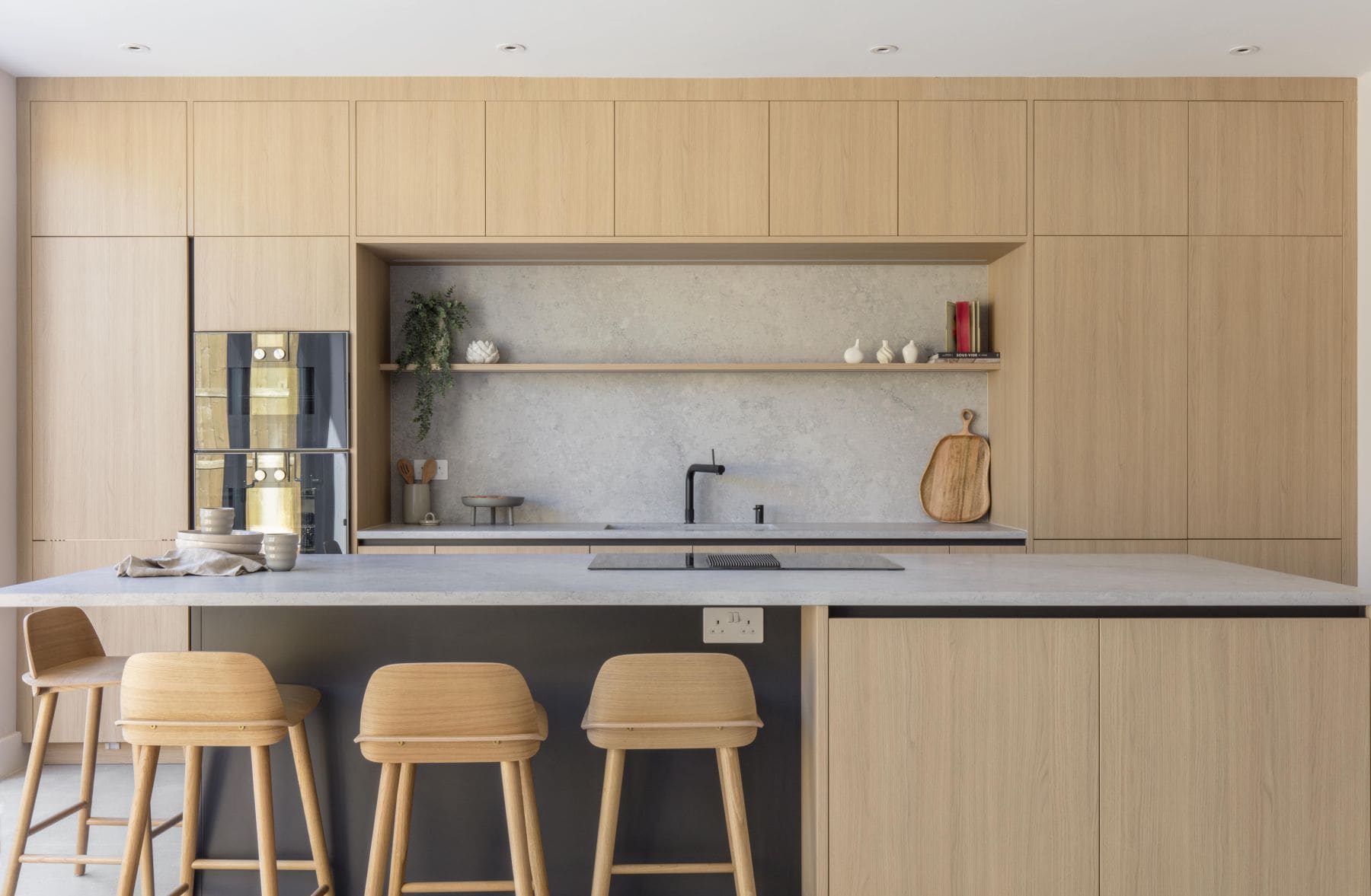 Sleek modern kitchen design by Randa Kort Interior Design in St Albans, Hertfordshire, featuring light wood cabinetry, minimalist decor, and a contemporary island with wooden stools.
